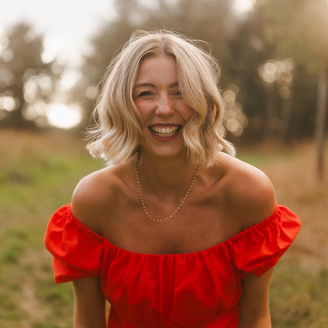 Marina Gears, vocal coach, laughing outdoors in a warm red top